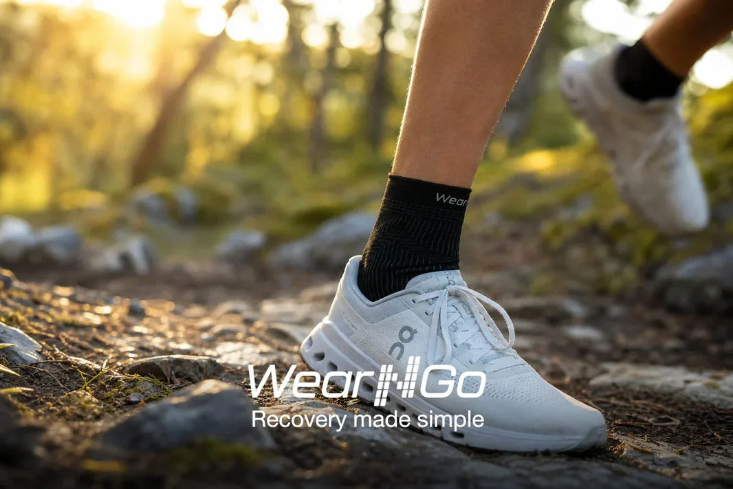 Wear'N'Go Ankelstøtte på jogger i norsk skogsti: sort knittet kompresjonshylse med Wear'N'Go-logo synlig over løpesko, morgenlys gjennom trærne