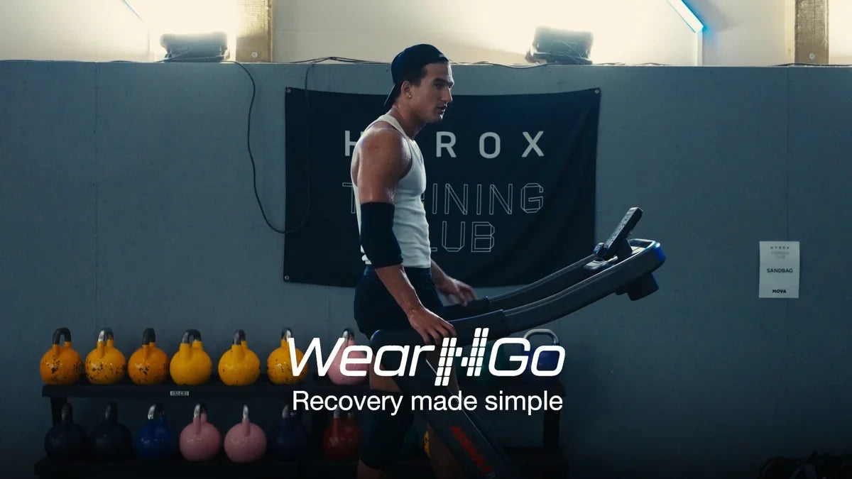 Løping på tredemølle foran en HYROX Training Club-vegg i et treningssenter, med Wear'N'Go armkompresjon-sleeve på armen